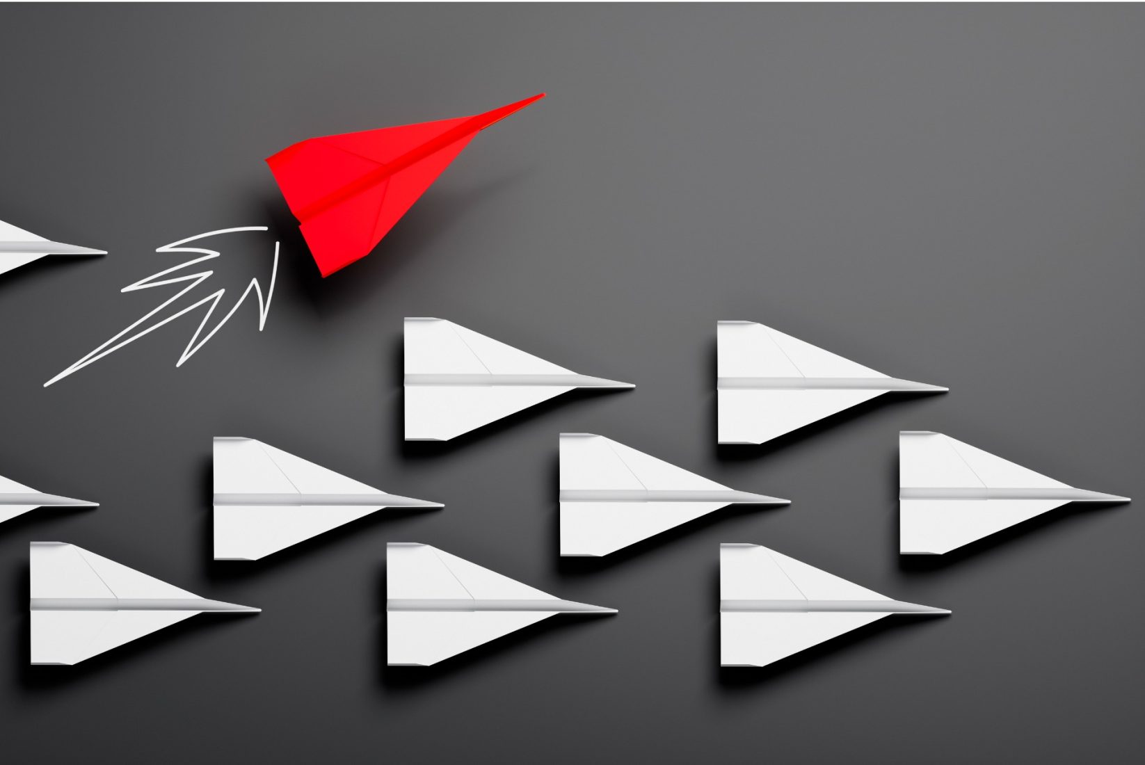 several white and one red paper aeroplane on a dark background as a symbol for competition